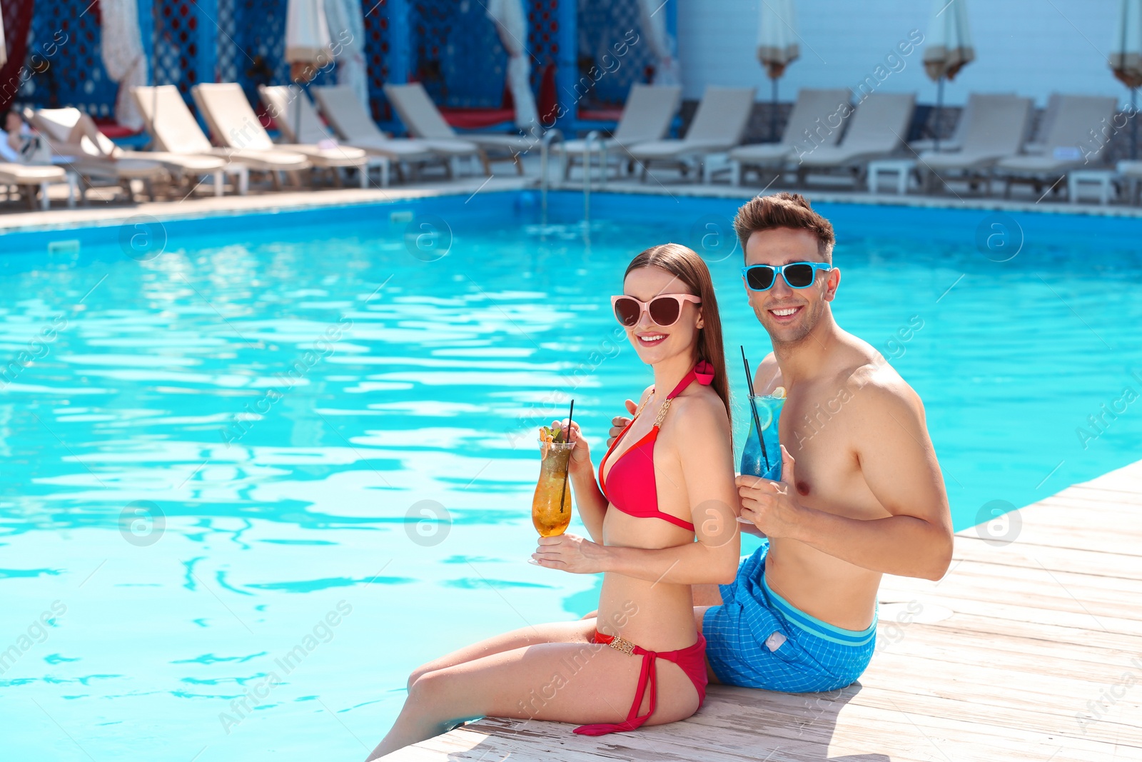 Photo of Happy young couple with cocktails near swimming pool