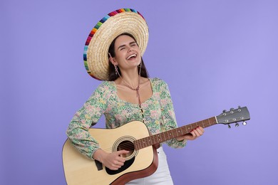 Photo of Young woman in Mexican sombrero hat playing guitar on violet background