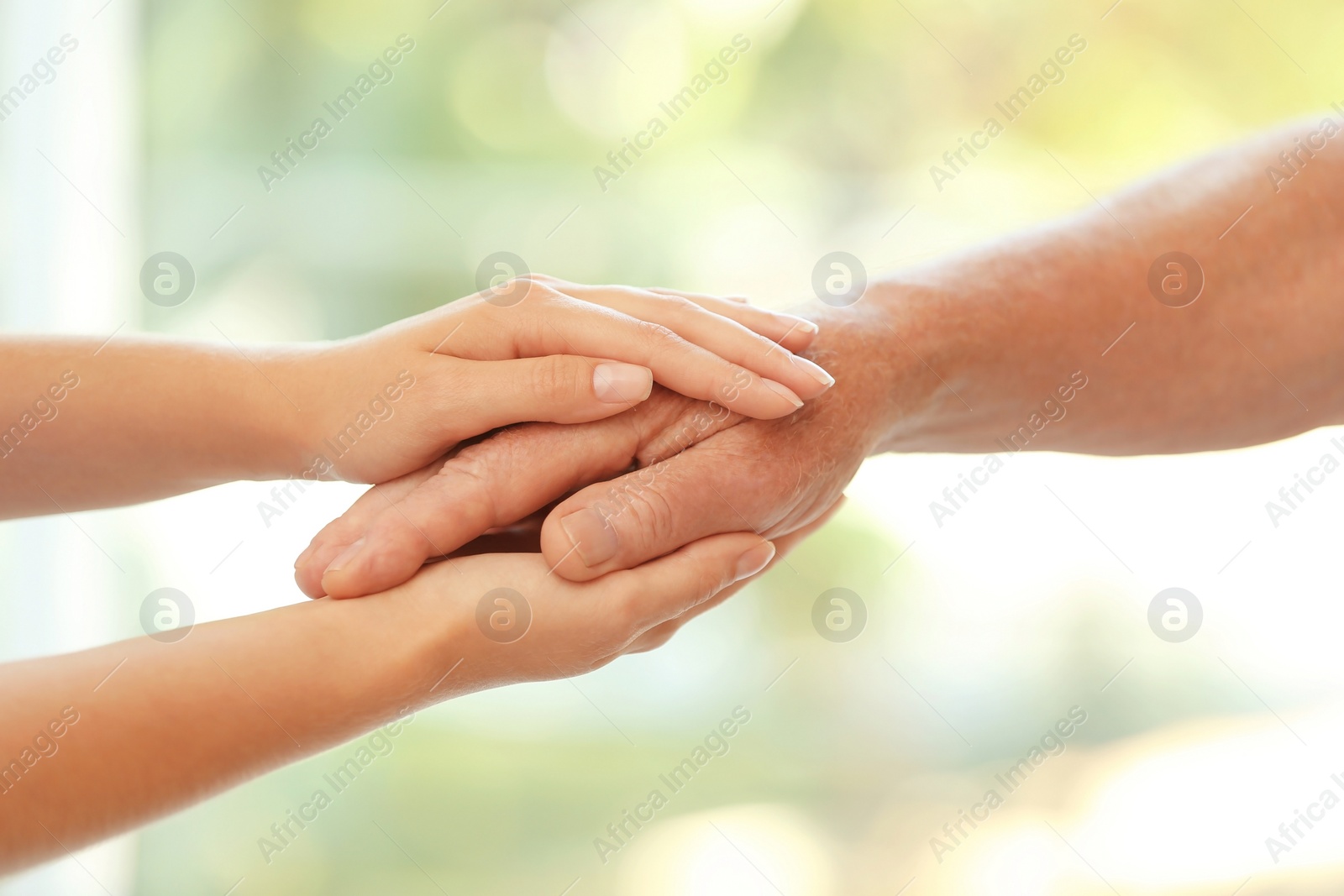 Photo of Young woman holding elderly man hand on blurred background, closeup. Help service