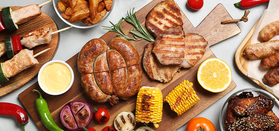 Flat lay composition with barbecued meat and vegetables on light table. Banner design