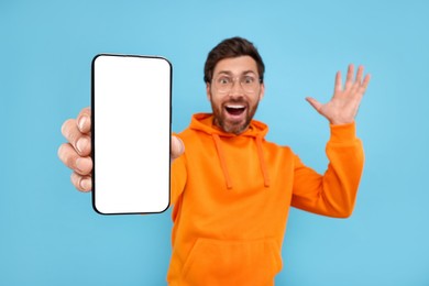 Photo of Surprised man showing smartphone in hand on light blue background, selective focus. Mockup for design