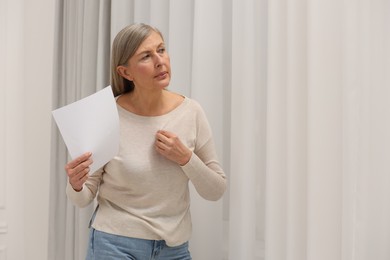 Menopause. Woman waving paper sheet to cool herself during hot flash at home, space for text