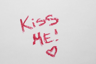 Photo of Phrase Kiss Me and red heart made of lipstick on white background