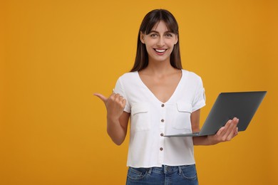 Photo of Special promotion. Happy woman with laptop pointing at something on orange background, space for text