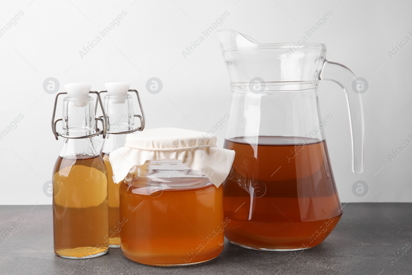 Photo of Homemade fermented kombucha in glass jar, jug and bottles on grey table