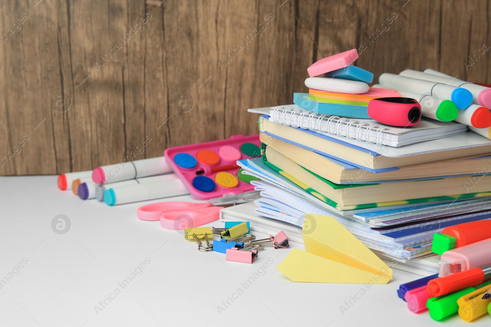 Photo of Many different books, paper plane and school stationery on white table, space for text. Back to school