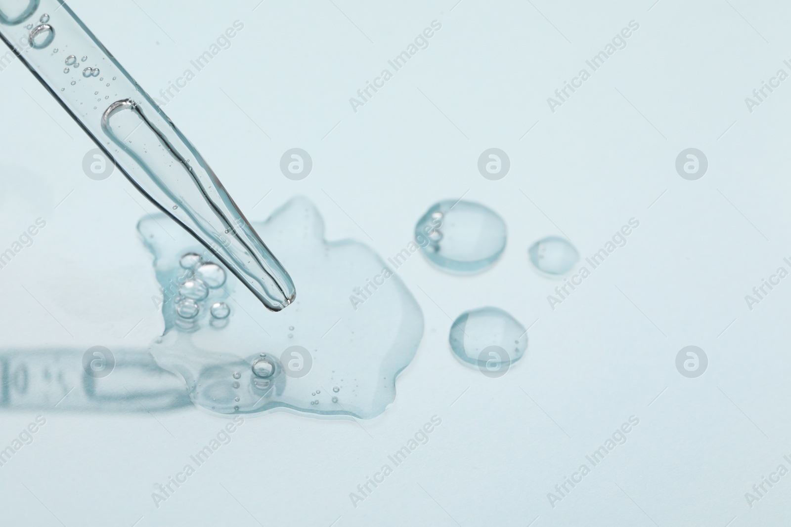 Photo of Glass pipette and transparent liquid on light background, closeup. Space for text