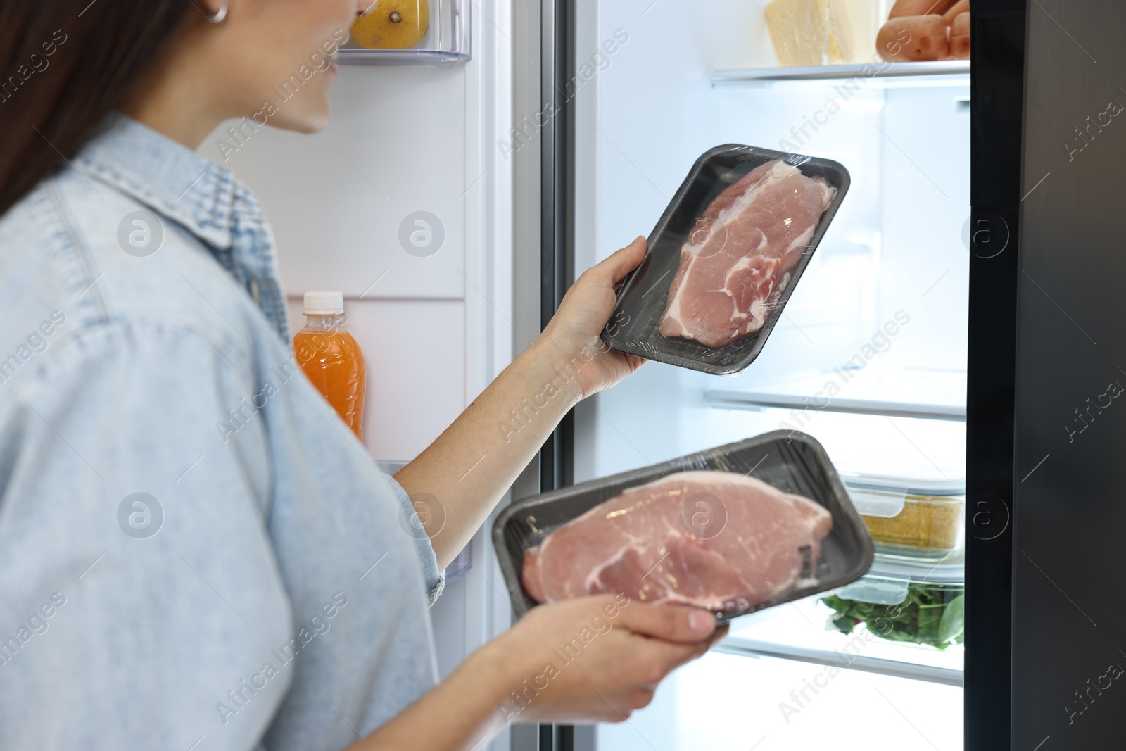 Photo of Young woman taking packs of meat out of refrigerator, closeup