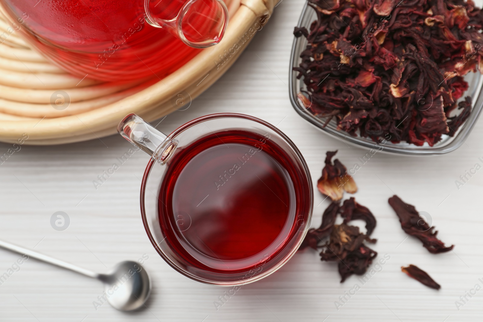 Photo of Delicious hibiscus tea and dry flowers on white wooden table, flat lay