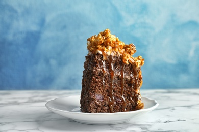 Photo of Piece of delicious homemade cake with caramel sauce and popcorn on table