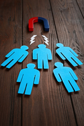 Photo of Magnet attracting paper people on wooden background