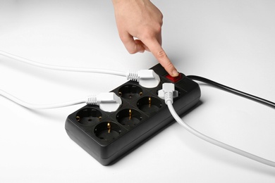 Woman pressing power button of extension cord on white background, closeup. Electrician's equipment