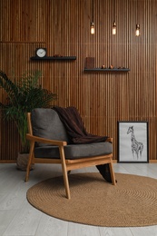 Photo of Stylish room interior with comfortable armchair and plant near wooden wall