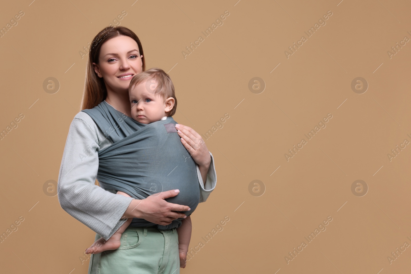 Photo of Mother holding her child in baby wrap on light brown background. Space for text