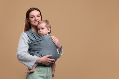 Mother holding her child in baby wrap on light brown background. Space for text