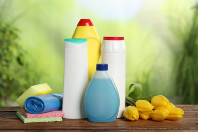 Photo of Spring cleaning. Different detergents, tools and beautiful flowers on wooden table outdoors