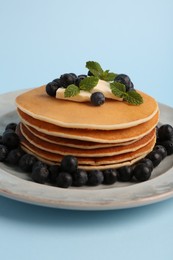 Stack of tasty pancakes with blueberries, butter and mint on light blue background, closeup