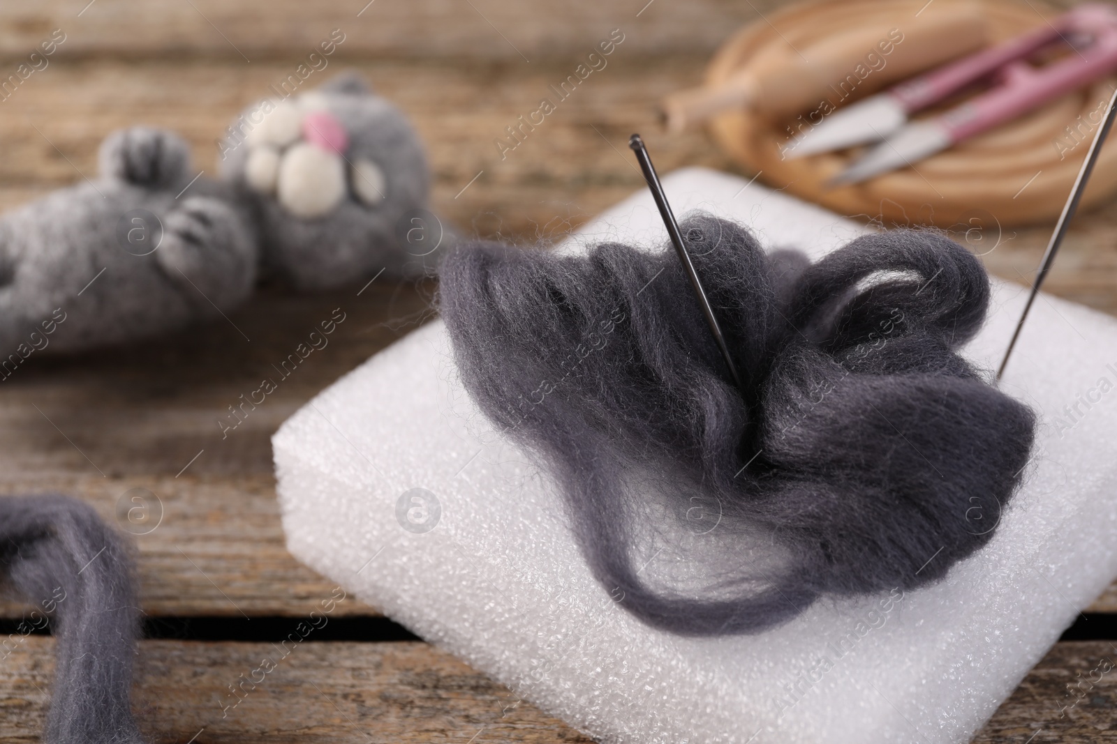 Photo of Grey felting wool, pad, needles and toy cat on wooden table, closeup