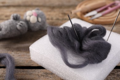 Grey felting wool, pad, needles and toy cat on wooden table, closeup