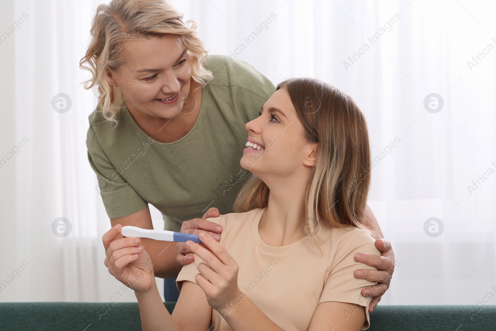 Photo of Young woman showing her mother pregnancy test at home. Grandparent reaction to future grandson