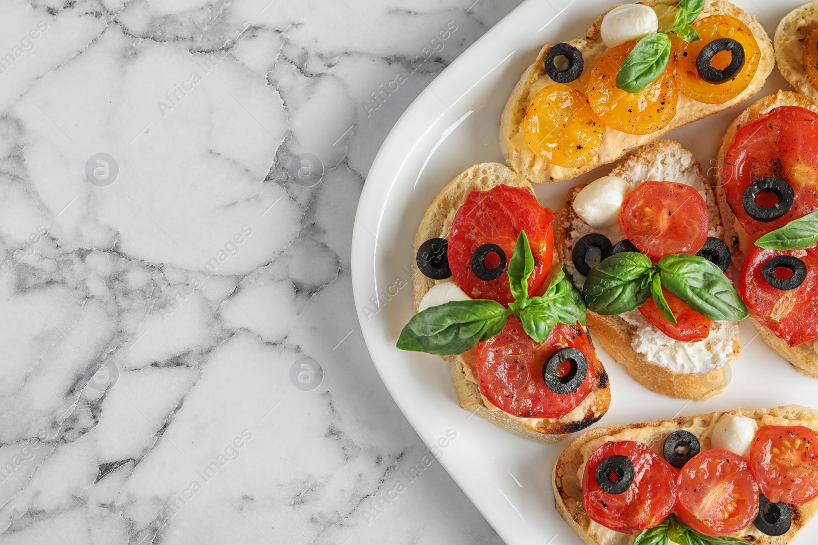 Photo of Plate of delicious tomato bruschettas on white marble background, top view. Space for text