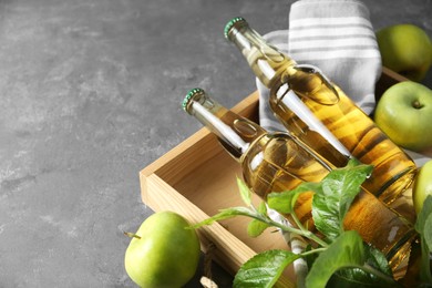 Photo of Delicious cider, ripe apples and green leaves on gray table, closeup. Space for text