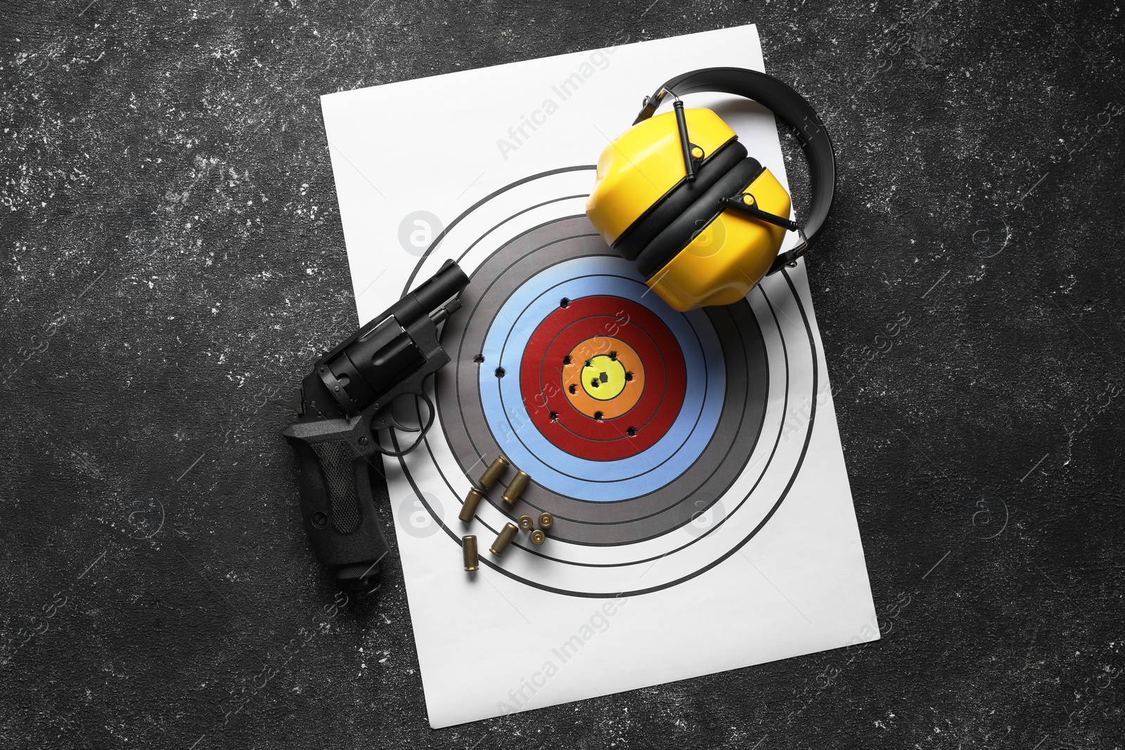 Photo of Shooting target, handgun and headphones on dark gray table, top view