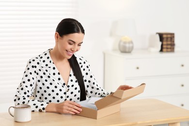 Happy woman holding greeting card near parcel with Christmas gift at home