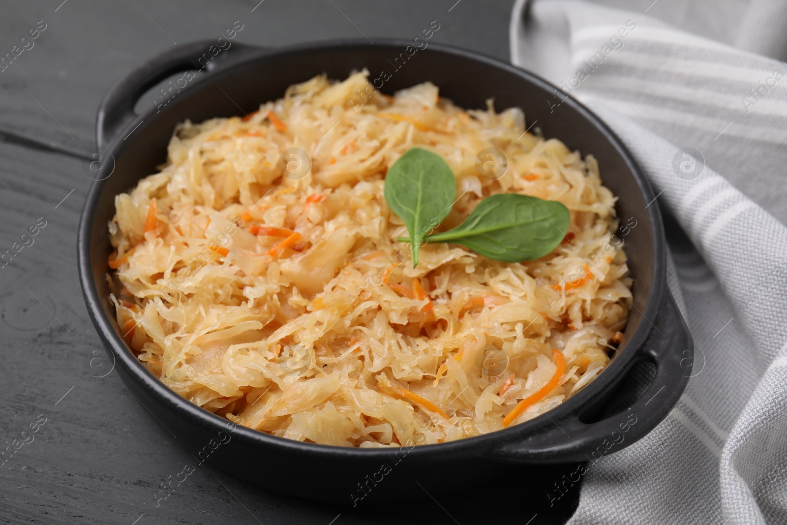 Photo of Serving pan with sauerkraut on black wooden table, closeup