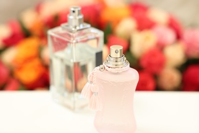 Photo of Bottles of perfume on white table against beautiful roses, closeup