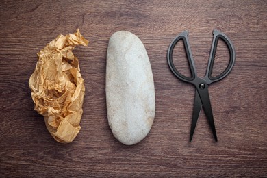 Photo of Rock, crumpled paper and scissors on wooden table, flat lay