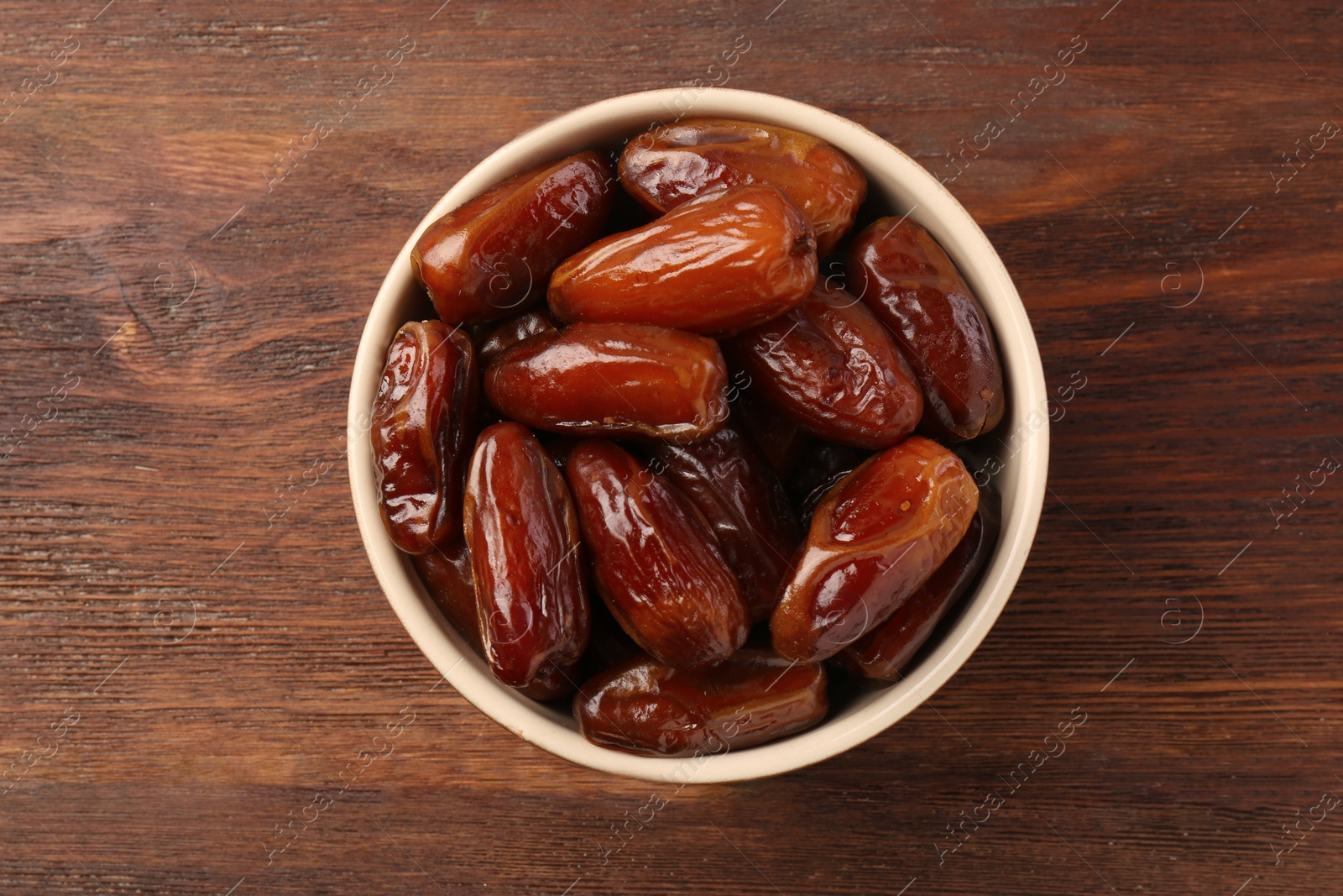 Photo of Sweet dried dates in bowl on wooden background, top view