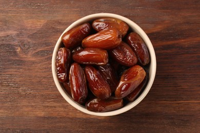 Photo of Sweet dried dates in bowl on wooden background, top view