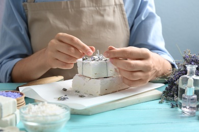 Photo of Woman decorating hand made soap bars with lavender flowers at light blue wooden table, closeup