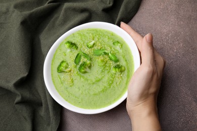 Photo of Woman with bowl of delicious broccoli cream soup at grey table, top view