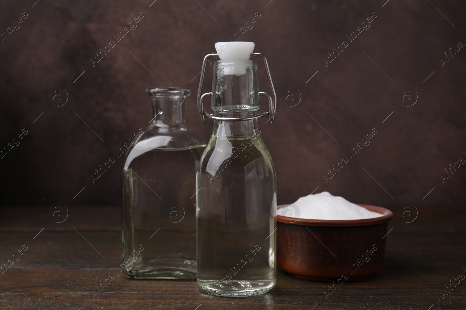 Photo of Vinegar in glass bottles and baking soda on wooden table