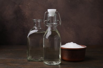 Photo of Vinegar in glass bottles and baking soda on wooden table