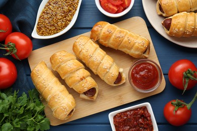 Photo of Delicious sausage rolls and ingredients on blue wooden table, flat lay