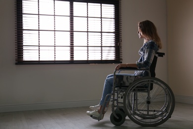 Photo of Young woman in wheelchair near window indoors