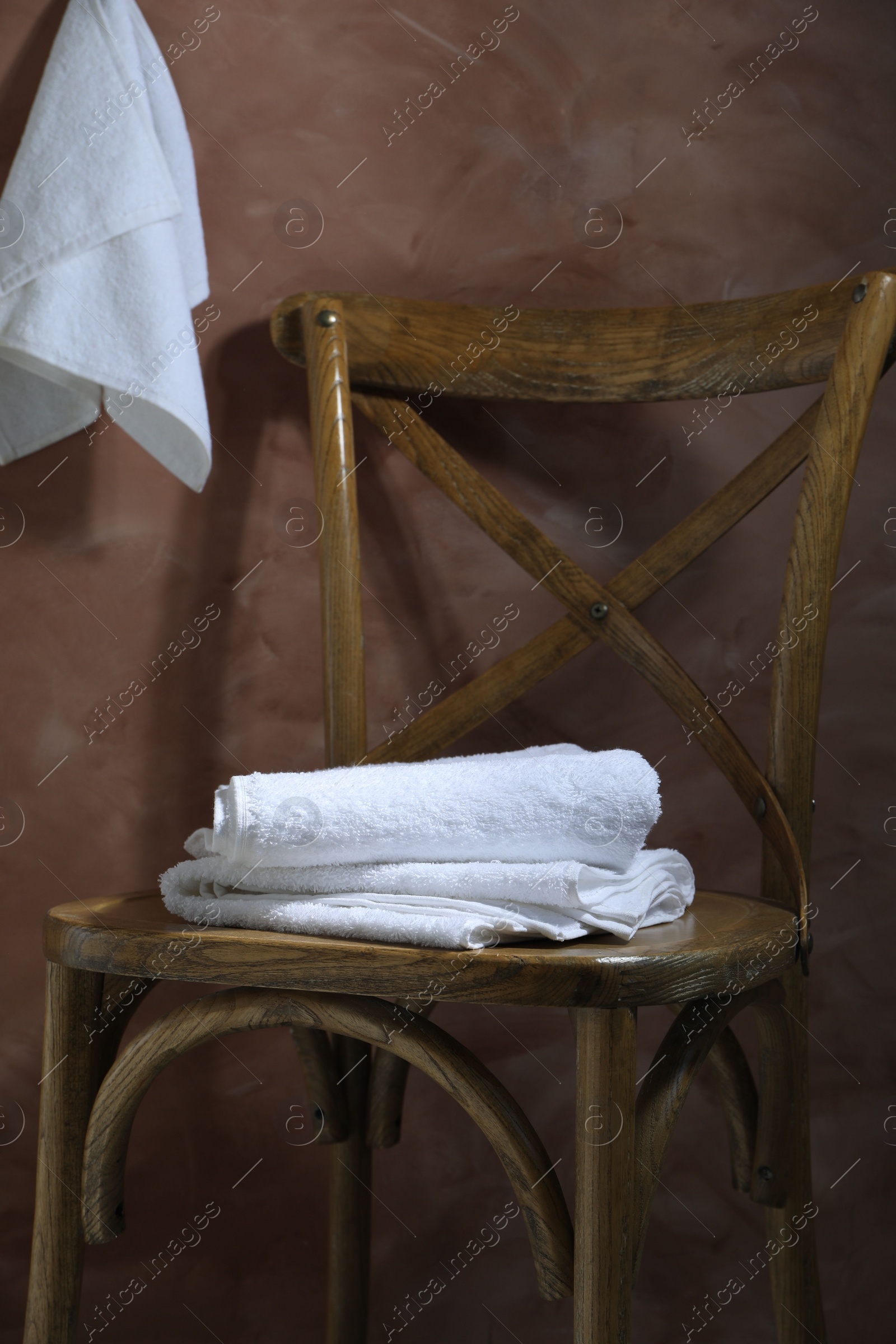 Photo of White terry towels on wooden chair against brown background