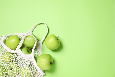 Photo of Net bag and fresh ripe apples on green background, flat lay. Space for text
