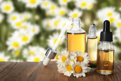 Image of Bottles of essential oil and chamomile flowers on wooden table against blurred background. Space for text