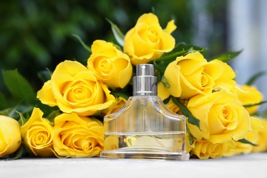 Photo of Perfume and beautiful bouquet of yellow roses on light table, closeup