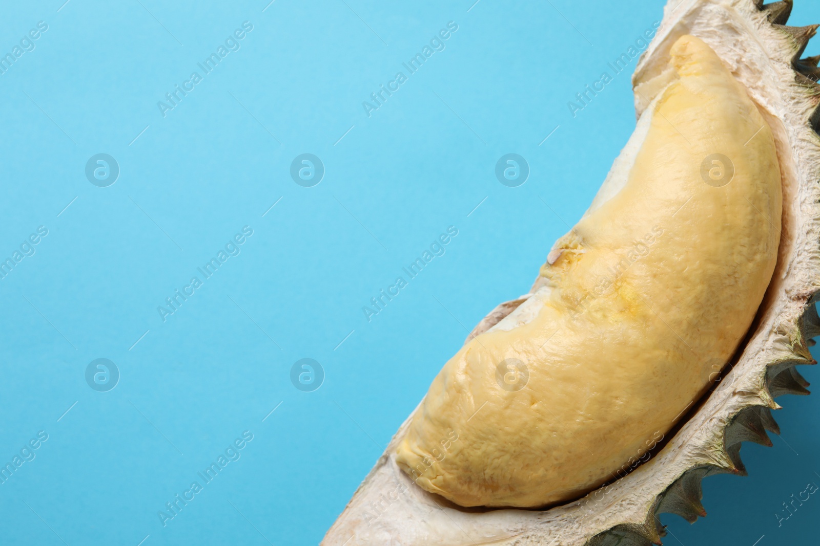 Photo of Piece of fresh ripe durian on light blue background, top view. Space for text