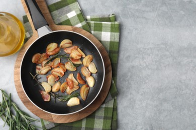 Frying pan with fried garlic cloves, rosemary and oil on gray table, flat lay. Space for text