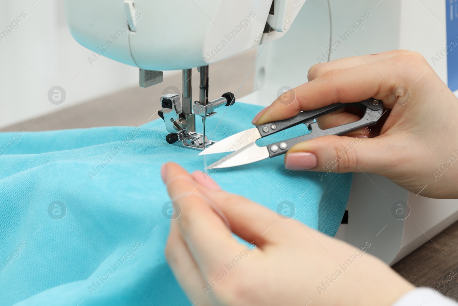 Photo of Seamstress with tailor's scissors working with sewing machine indoors, closeup