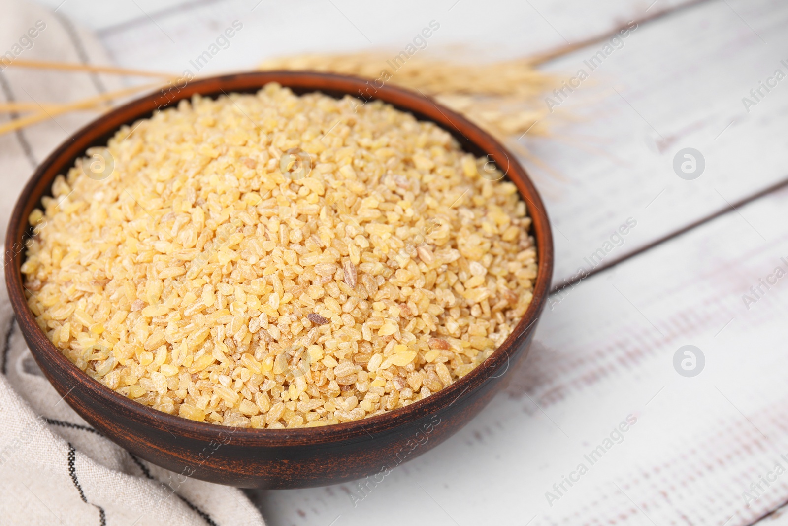 Photo of Raw bulgur in bowl on white wooden table, closeup