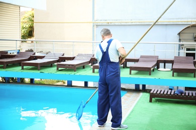 Photo of Male worker cleaning outdoor pool with scoop net