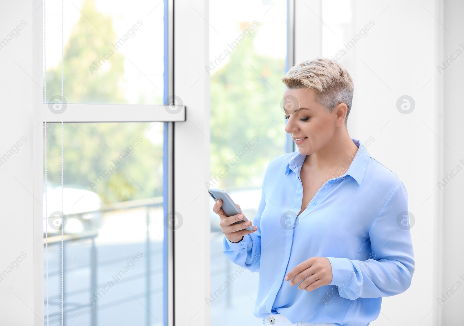 Photo of Portrait of attractive business woman using mobile phone near window at office