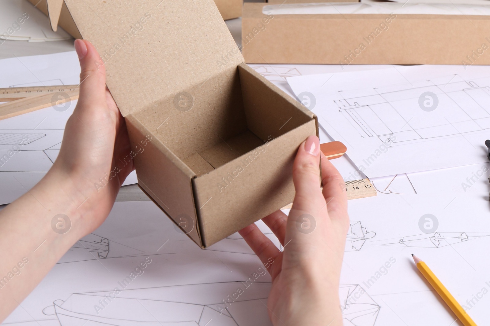 Photo of Woman holding cardboard box near drawings at table, closeup